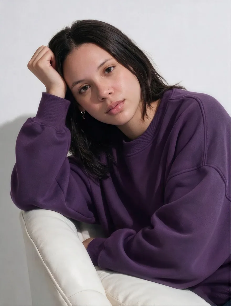 Emilly Silva de moletom roxo, apoiada numa poltrona branca